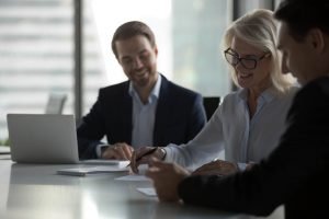 Smiling middle aged businesswoman signing paper contract at group meeting